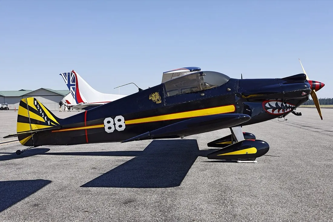 A black Monnett Sonerai II homebuilt with yellow and red trim and a shark-mouth nose, parked on a ramp