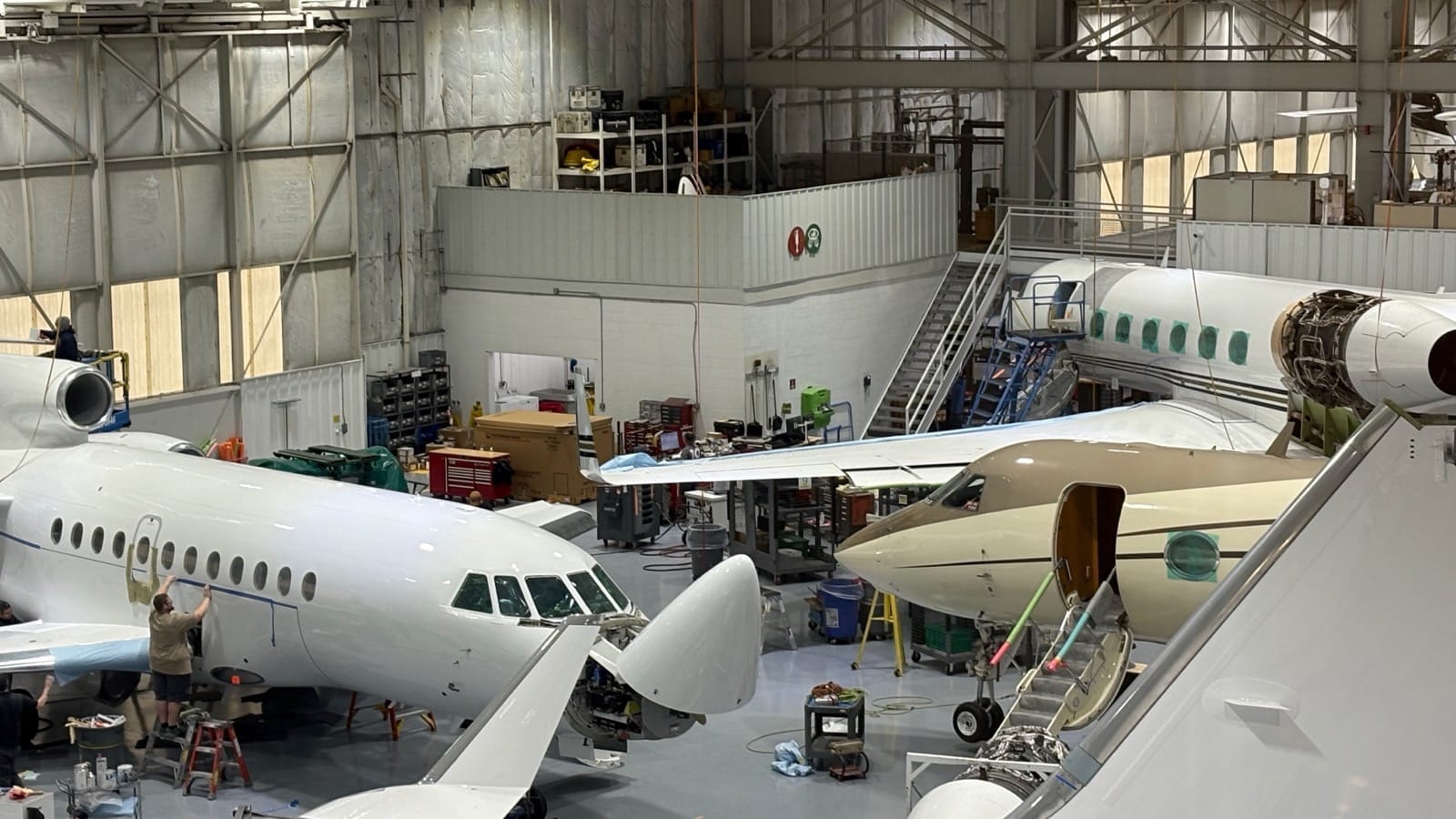 A Duncan Aviation technician working on a business jet fuselage in a hangar packed with aircraft under maintenance