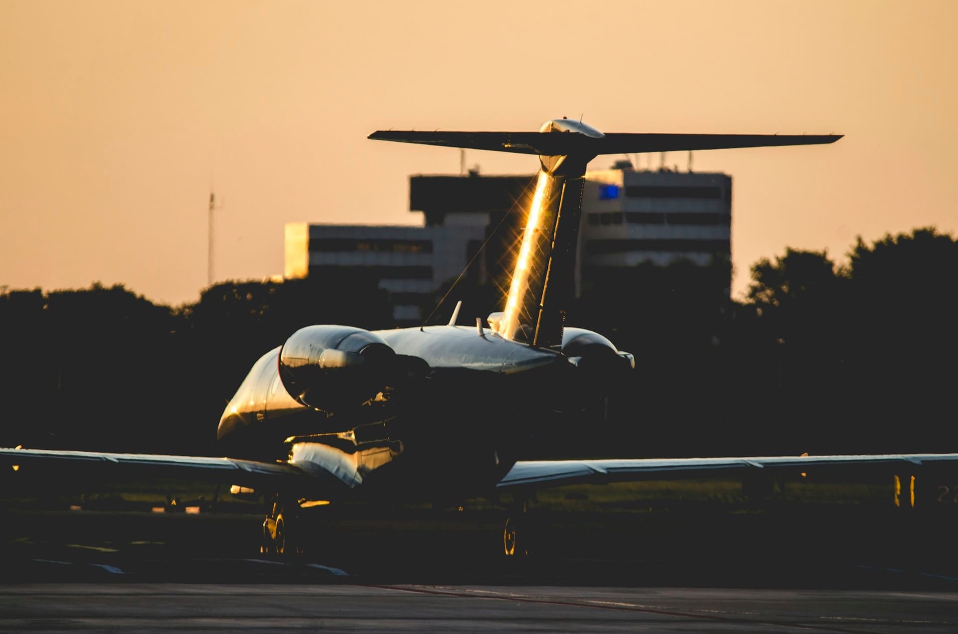 Business jet on the ground at dusk, backlit, with an airport terminal and control tower behind it